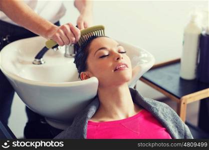 beauty and people concept - happy young woman with hairdresser combing wet hair after washing at salon. happy young woman at hair salon
