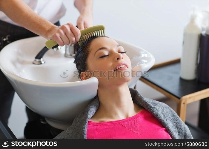 beauty and people concept - happy young woman with hairdresser combing wet hair after washing at salon