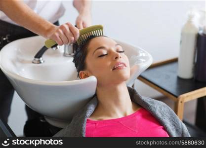 beauty and people concept - happy young woman with hairdresser combing wet hair after washing at salon