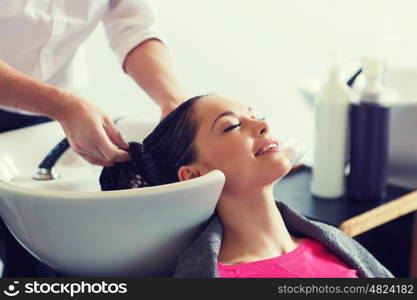 beauty and people concept - happy young woman with hairdresser washing head at hair salon. happy young woman at hair salon