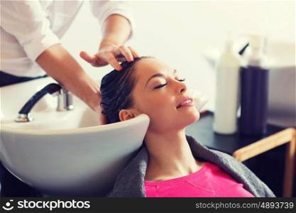 beauty and people concept - happy young woman with hairdresser washing head at hair salon. happy young woman at hair salon
