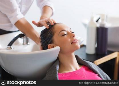 beauty and people concept - happy young woman with hairdresser washing head at hair salon. happy young woman at hair salon