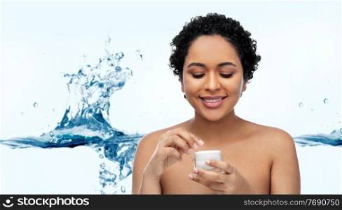 beauty and people concept - portrait of african american woman with bare shoulders holding jar of moisturizer over white background with bubbles in blue water splash. young african american woman with moisturizer