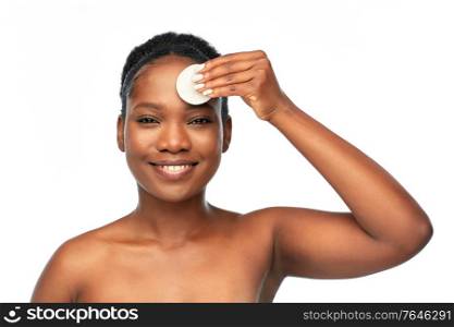 beauty and people concept - portrait of happy smiling young african american woman with bare shoulders cleaning her face with cotton pad over white background. african woman cleaning face with cotton pad