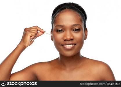 beauty and people concept - portrait of happy smiling young african american woman with bare shoulders cleaning ear with cotton swab over white background. happy african woman cleaning ear with cotton swab