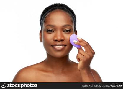 beauty and people concept - portrait of happy smiling young african american woman with bare shoulders with make up blending sponge over white background. african american woman with make up sponge