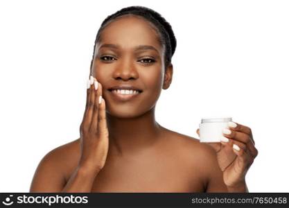 beauty and people concept - portrait of happy smiling young african american woman with bare shoulders applying moisturizer to her face over white background. smiling african american woman with moisturizer