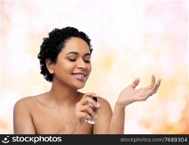 beauty and people concept - portrait of happy smiling young african american woman with bare shoulders with perfume over lights background. young african american woman with perfume