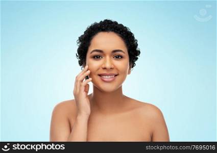 beauty and people concept - portrait of happy smiling young african american woman with bare shoulders touching her face over blue background. portrait of young african american woman