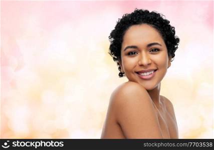 beauty and people concept - portrait of happy smiling young african american woman with bare shoulders over festive lights on pink background. portrait of young african american woman