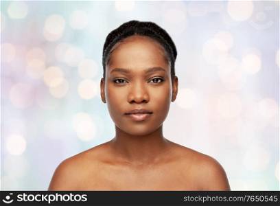 beauty and people concept - portrait of young african american woman with bare shoulders over holidays lights on blue background. portrait of young african american woman