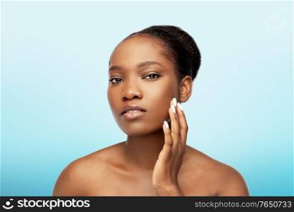 beauty and people concept - portrait of young african american woman with bare shoulders touching her face over blue background. portrait of african woman touching her face