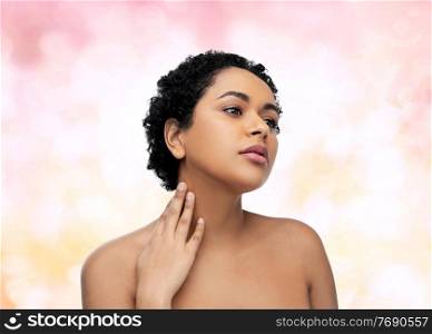 beauty and people concept - portrait of young african american woman with bare shoulders over pink lights background. portrait of young african american woman