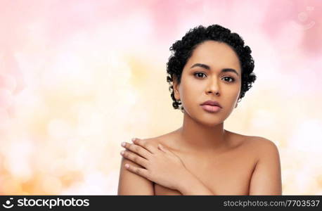 beauty and people concept - portrait of young african american woman with bare shoulders over festive lights on pink background. portrait of young african american woman