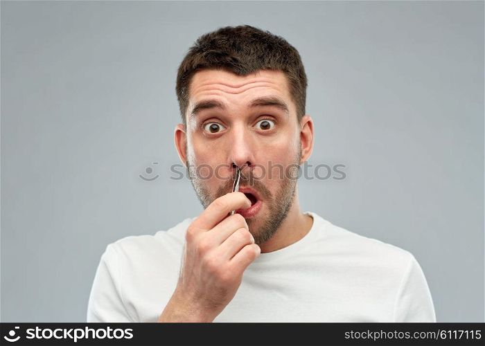 beauty and people concept - smiling young man with tweezers tweezing hair frome nose over gray background. man with tweezers tweezing hair from nose
