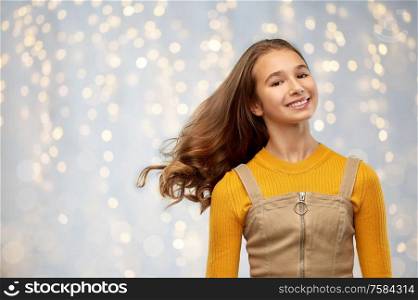 beauty and people concept - smiling young teenage girl with waving long hair over festive lights background. young teenage girl with waving long hair