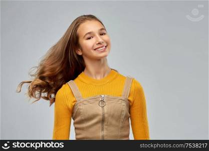 beauty and people concept - smiling young teenage girl with waving long hair over grey background. young teenage girl with waving long hair