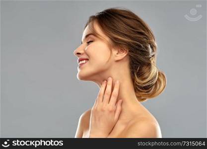 beauty and people concept - smiling young woman touching her neck over grey background. smiling young woman touching her neck