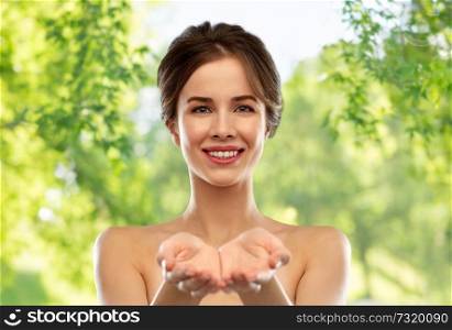 beauty and people concept - smiling young woman with bare shoulders holding something imaginary over green natural background. smiling young woman holding something imaginary