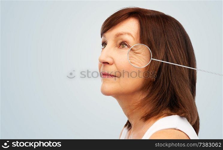 beauty and skin aging concept - portrait of senior woman with zoomed eye wrinkles in pointer over grey background. senior woman with zoomed eye wrinkles