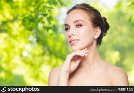 beauty and skin care concept - beautiful young woman touching her face over green natural background. beautiful young woman touching her face. beautiful young woman touching her face