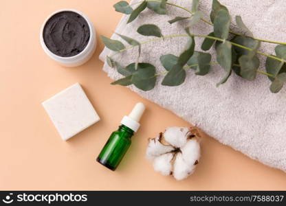 beauty and spa concept - serum or essential oil, mask, soap bar, eucalyptus cinerea and cotton flower on bath towel. serum, clay mask, oil and eucalyptus on bath towel