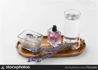 beauty and wellness concept - sea salt, perfume, lavender and glass of water on wooden tray. sea salt, perfume and lavender on wooden tray