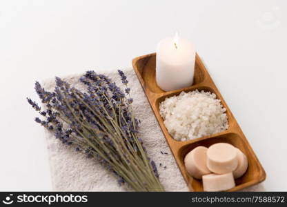 beauty and wellness concept - sea salt, soap and candle on wooden tray and bunch of lavender on bath towel. sea salt, soap, candle and lavender on bath towel