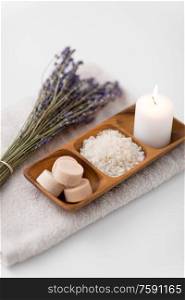 beauty and wellness concept - sea salt, soap and candle on wooden tray and bunch of lavender on bath towel. sea salt, soap, candle and lavender on bath towel