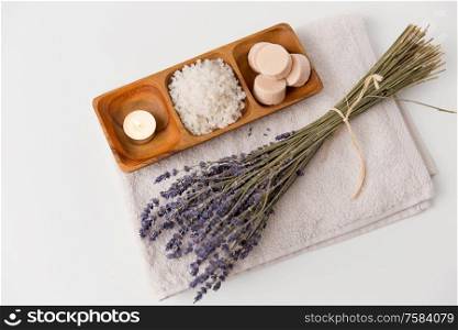 beauty and wellness concept - sea salt, soap and tea candle on wooden tray and bunch of lavender on bath towel. sea salt, soap, candle and lavender on bath towel