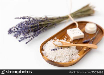 beauty and wellness concept - sea salt with spoon, lavender, soap bar and moisturizer on wooden tray. sea salt with spoon and lavender on wooden tray