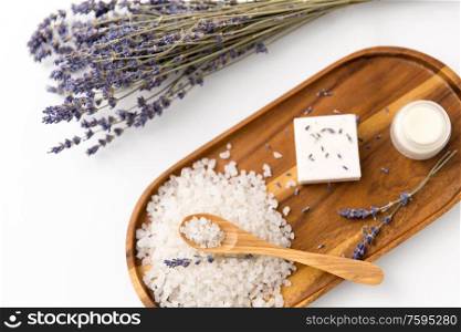 beauty and wellness concept - sea salt with spoon, soap, moisturizer, lavender and cotton flowers on wooden tray. sea salt, lavender soap and moisturizer on tray