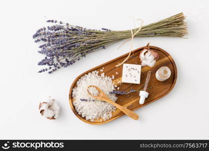 beauty and wellness concept - sea salt with spoon, soap, serum with dropper, lavender and cotton flowers on wooden tray. sea salt, lavender soap and serum on wooden tray