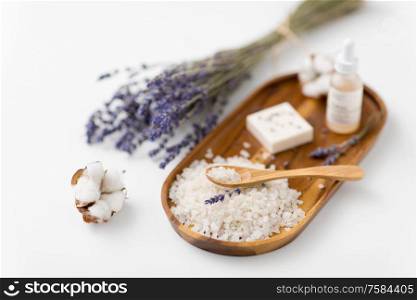 beauty and wellness concept - sea salt with spoon, soap, serum with dropper, lavender and cotton flowers on wooden tray. sea salt, lavender soap and serum on wooden tray