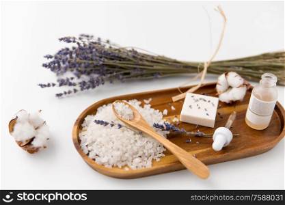 beauty and wellness concept - sea salt with spoon, soap, serum with dropper, lavender and cotton flowers on wooden tray. sea salt, lavender soap and serum on wooden tray