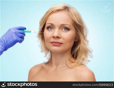 beauty, anti-aging cosmetic surgery concept - middle aged woman face and beautician hand in glove with syringe making injection to cheek over blue background