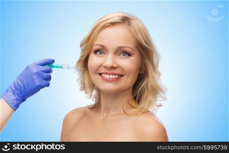 beauty, anti-aging cosmetic surgery concept - smiling middle aged woman face and beautician hand in glove with syringe making injection to cheek over blue background