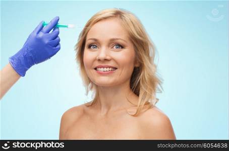 beauty, anti-aging cosmetic surgery concept - smiling woman face and beautician hand in glove with syringe making injection to forehead over blue background