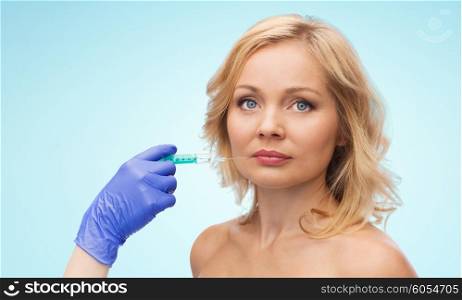 beauty, anti-aging cosmetic surgery concept - woman face and beautician hand in glove with syringe making injection to lips over blue background