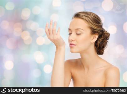 beauty, aroma, people and body care concept - young woman smelling perfume from wrist of her hand over blue holidays lights background