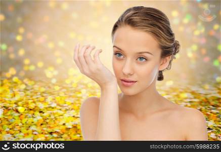 beauty, aroma, people and body care concept - young woman smelling perfume from wrist of her hand over yellow glitter and confetti background