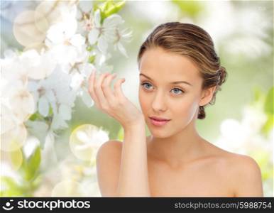 beauty, aroma, people and body care concept - young woman smelling perfume from wrist of her hand over green natural cherry blossom background