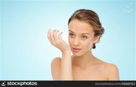 beauty, aroma, people and body care concept - young woman smelling perfume from wrist of her hand over blue background