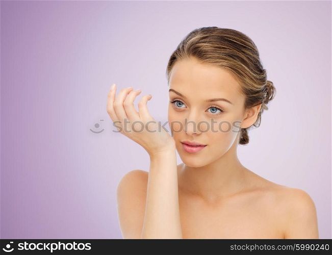 beauty, aroma, people and body care concept - young woman smelling perfume from wrist of her hand over violet background