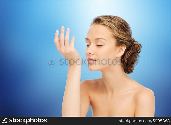 beauty, aroma, people and body care concept - young woman smelling perfume from wrist of her hand over marine blue background