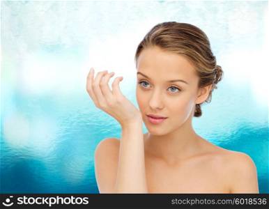 beauty, aroma, people and body care concept - young woman smelling perfume from wrist of her hand over blue water background