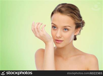 beauty, aroma, people and body care concept - young woman smelling perfume from wrist of her hand over green natural background
