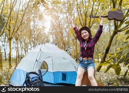 Beauty Asian woman holding guitar and raising hands in forest. Pine woods background. People and lifestyles concet. Camping and travel concept
