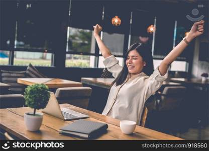 Beauty Asian woman raising two hands after finishing job happily with laptop computer. People and lifestyles concept. Technology and Business working theme. Occupation and coffee shop theme.