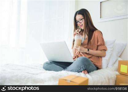 Beauty Asian woman using laptop and drinking coffee on bed. Business and Technology concept. Delivery and Online shopping concept. Post and Service theme.
